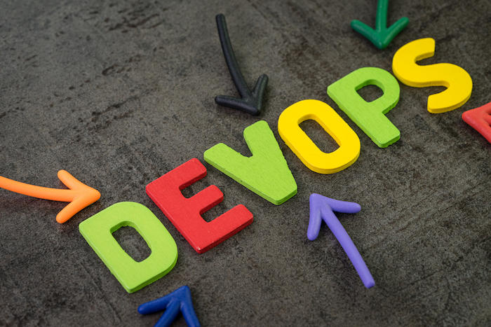 Devops for software continuous operations and development or programming concept, multi color arrows pointing to the word Devops at the center of black cement chalkboard wall