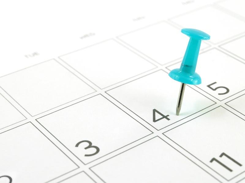 close up single blue plastic push pin tacking in schedule box of 4th of July on white desk calendar page