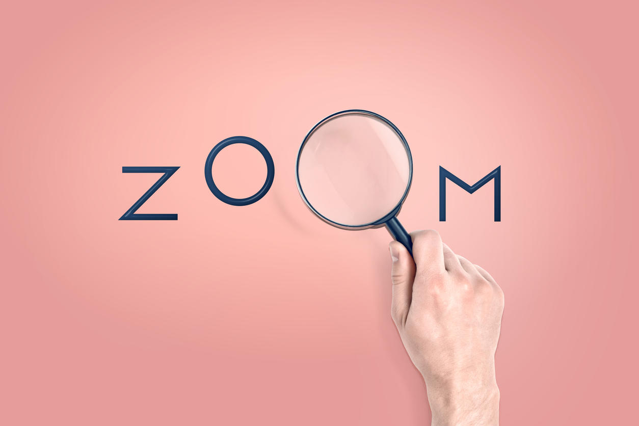 Male hand holds a large magnifying glass which serves as a letter in a word ZOOM.