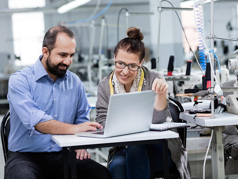 Adult man and woman working with computer in textile factory.