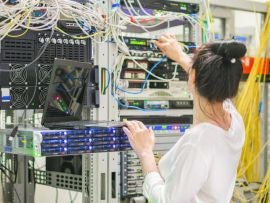 The girl works in the server room.The woman switches the wires in the datacenter.