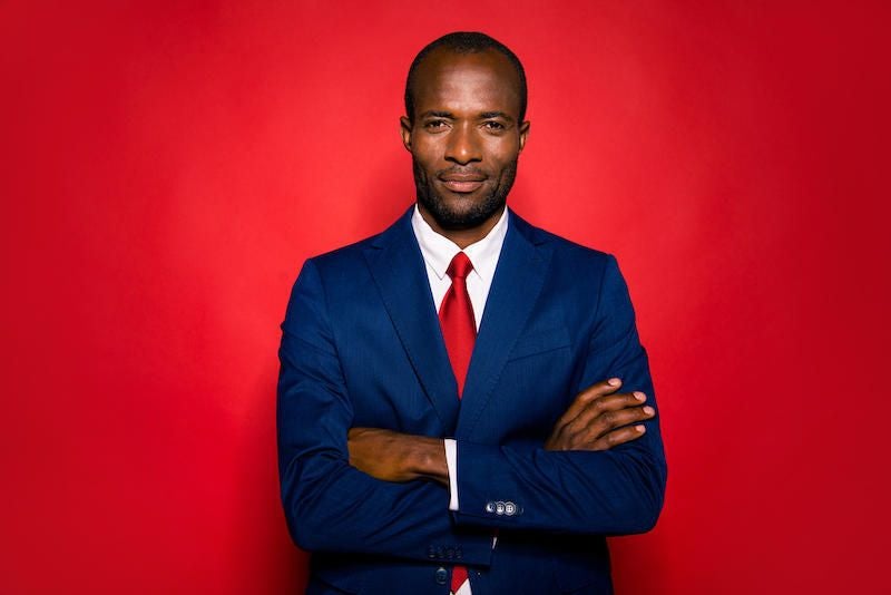 Portrait of nice positive calm experienced smart clever well-groomed attractive handsome content mulatto man folded arms in suit isolated over bright vivid red background