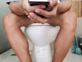 Asian guy using mobile phone while sitting in toilet