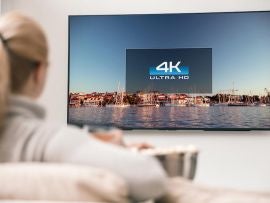 Big modern TV with 4k resolutions and young woman on foreground watching some video