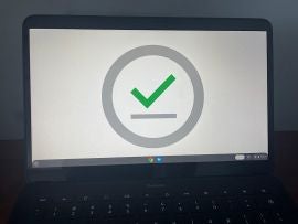 Photo of a Pixelbook Go with wallpaper set to a green checkmark with a gray underline, surrounded by a gray circle.
