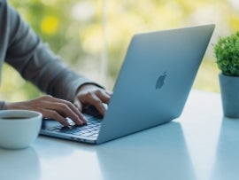 A woman using and typing on Apple MacBook Pro laptop computer on the table in office.