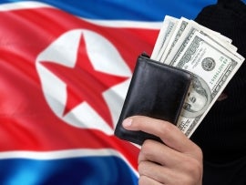 North Korea security and crime concept. Black criminals wear a head yarn, hold a dollar banknotes on national background.