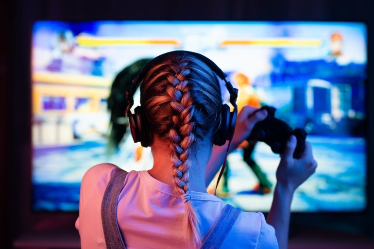 A gamer or a streamer girl at home in a dark room with a gamepad playing with friends on the networks in video games. A young man sits in front of a monitor or TV.