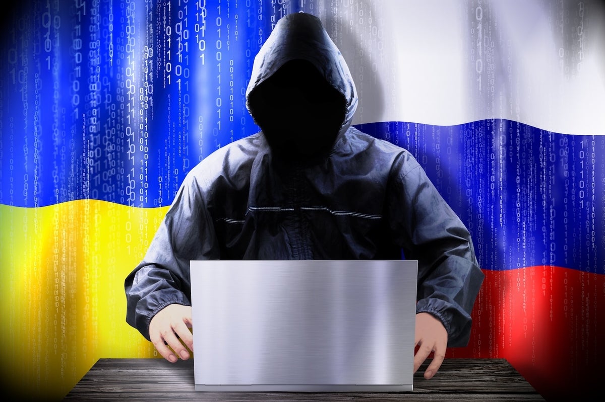Anonymous hacker working on a laptop, flags of Ukraine and Russia