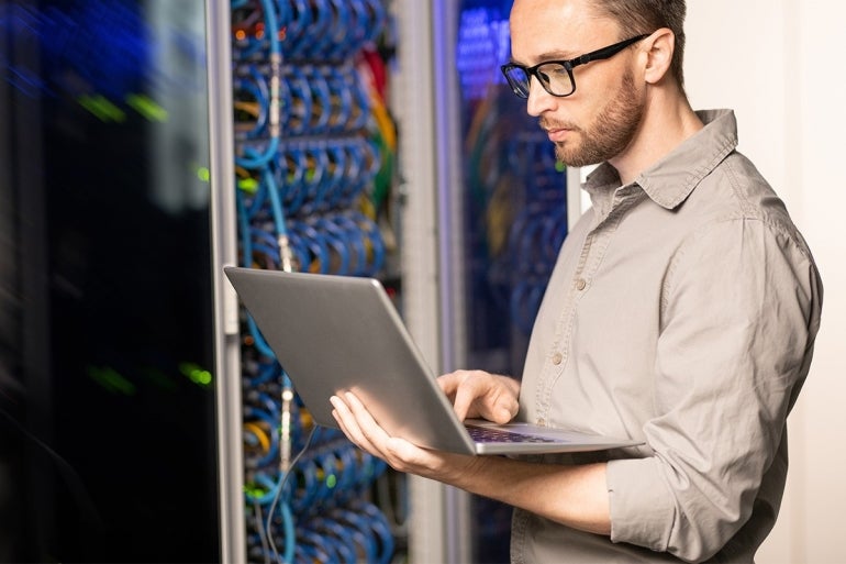 man holding an open laptop next to networking infrastructure