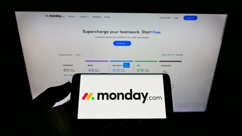Person holding mobile phone with logo of company Monday.com Ltd. on screen in front of web page.