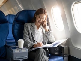 Business young asian woman talking on phone during working for paperwork financial report on airplane, flight in plane