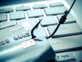 A hook pulls a credit card across a computer keyboard.