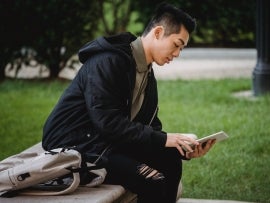 A person reading on a tablet on a bench.
