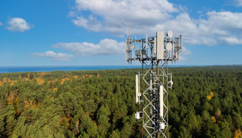 telecommunication tower with antennas for 5g network on forest and blue sky background