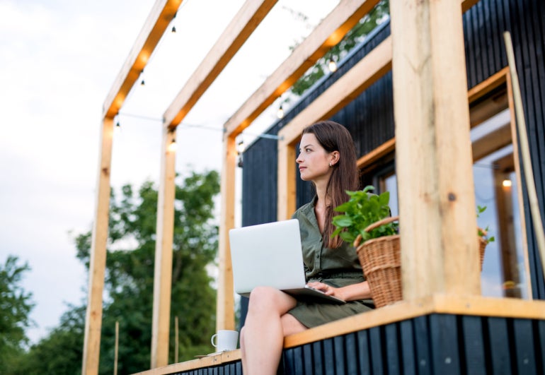 Young woman with laptop outdoors, weekend away in container house in countryside.