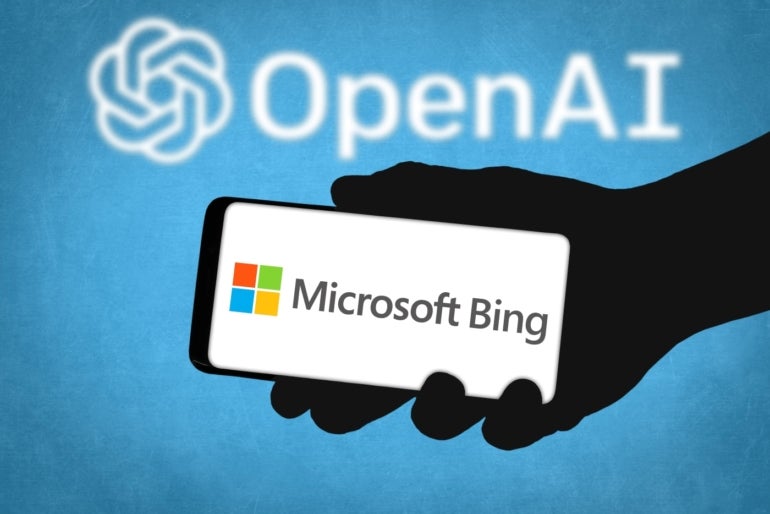 Shadowy hand holding a smartphone with Microsoft Bing on it over a blue background with the OpenAI logo