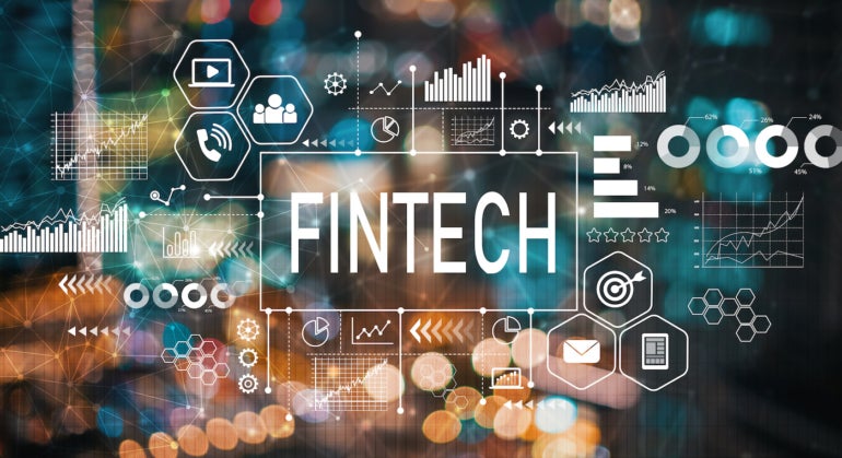 The word Fintech with finance symbols over a blurry background.