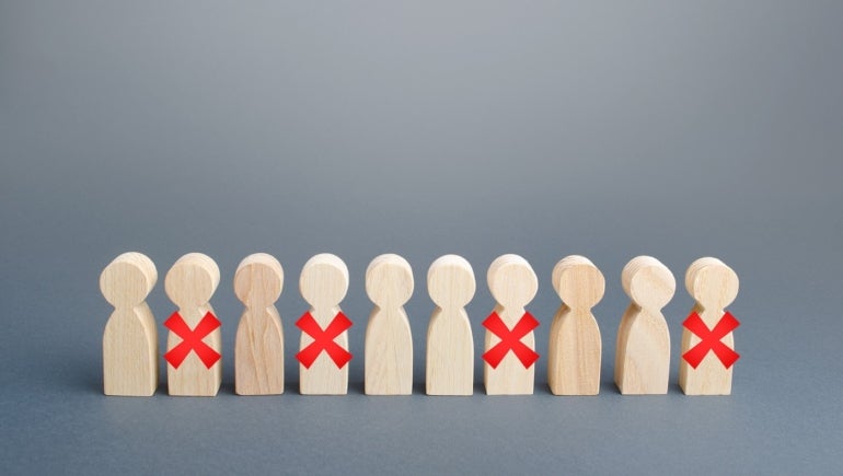 This photo illustrates employee layoffs using Xs over wooden figures.