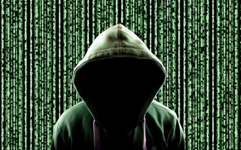 A hooded individual is completely in shadow and has a green background of binary code behind them.