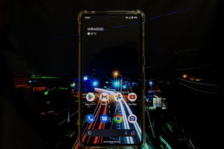 A smart phone with several apps displayed. The phone's background looks like a night sky and a multicolored, lit street; this imagery is also visible in the image background.