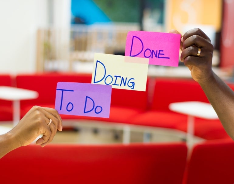 Two hands holding kanban sticky notes that say, "to do, doing, done."